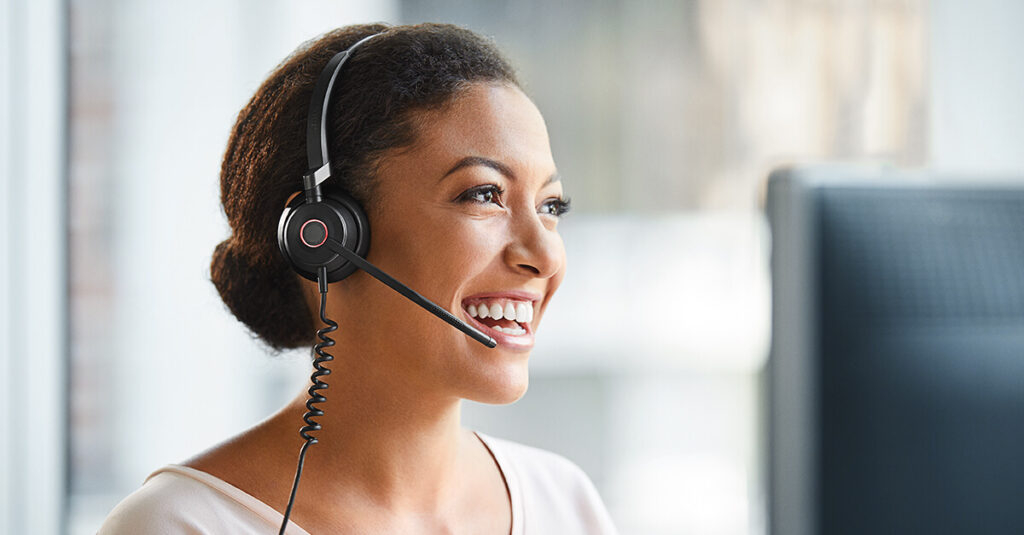 Smiling woman in call centre wearing a headset helping a business set up a 1300 number